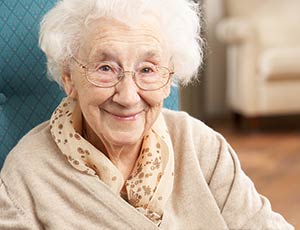 Older woman, seated, smiling at the viewer.